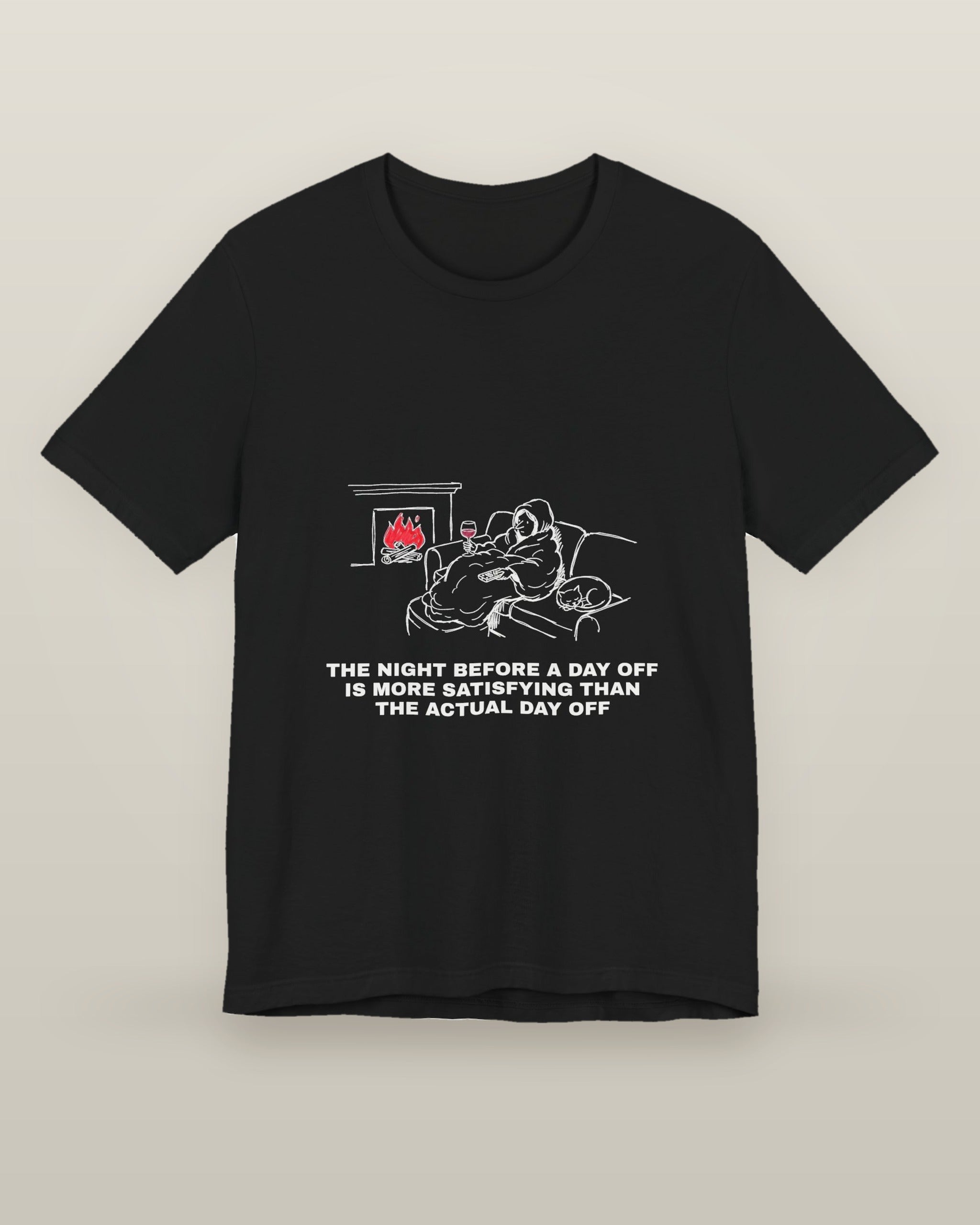 The night before a day off is more satisfying than the actual day off — a hooded figure under a blanket with wine, a remote, a sleeping cat and a lit fire, printed on a black cotton t-shirt, front view