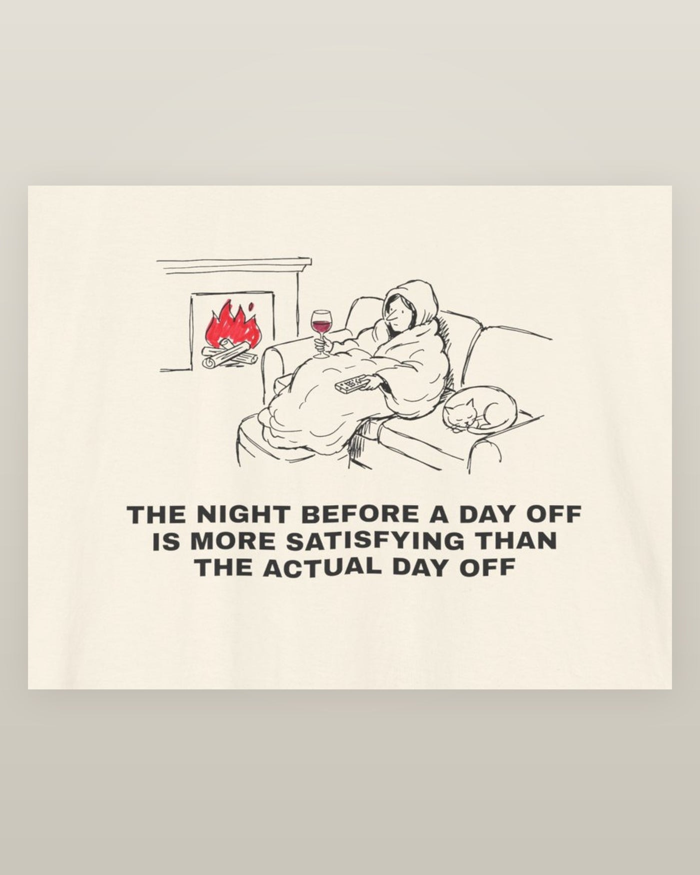 The night before a day off is more satisfying than the actual day off — a hooded figure under a blanket with wine, a remote, a sleeping cat and a lit fire, printed on a natural cream cotton t-shirt, close detail of the print