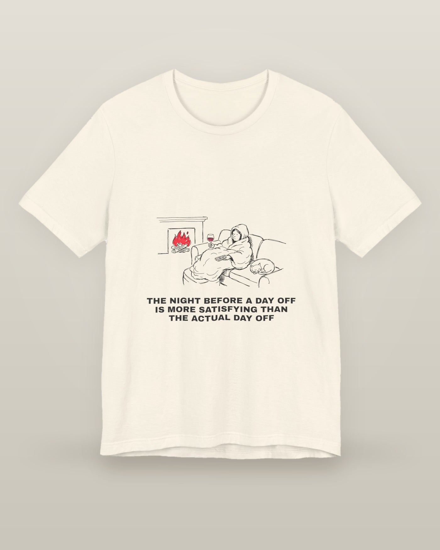 The night before a day off is more satisfying than the actual day off — a hooded figure under a blanket with wine, a remote, a sleeping cat and a lit fire, printed on a natural cream cotton t-shirt, front view