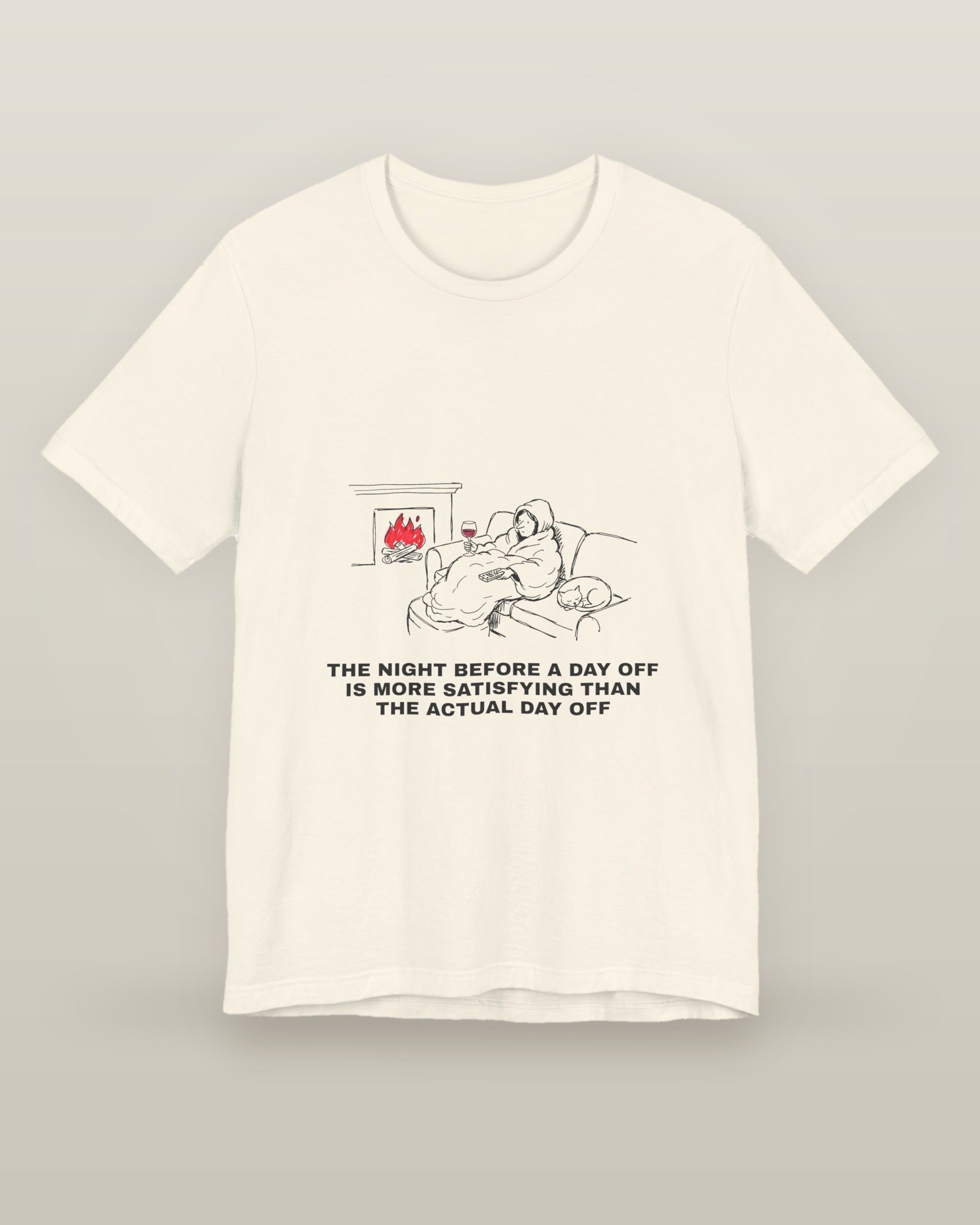 The night before a day off is more satisfying than the actual day off — a hooded figure under a blanket with wine, a remote, a sleeping cat and a lit fire, printed on a natural cream cotton t-shirt, front view