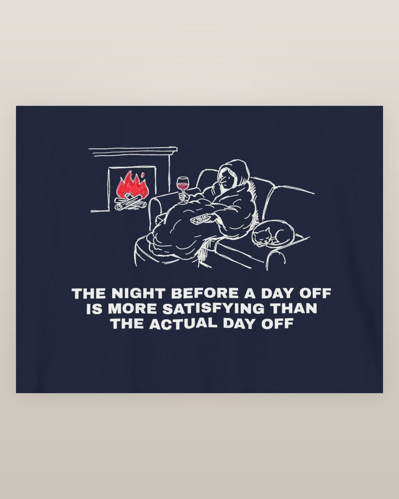 The night before a day off is more satisfying than the actual day off — a hooded figure under a blanket with wine, a remote, a sleeping cat and a lit fire, printed on a navy cotton t-shirt, close detail of the print