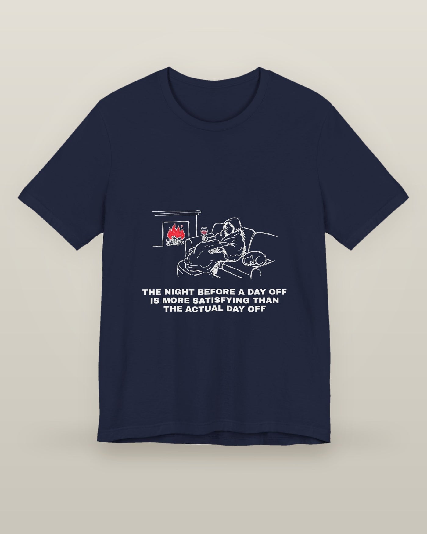 The night before a day off is more satisfying than the actual day off — a hooded figure under a blanket with wine, a remote, a sleeping cat and a lit fire, printed on a navy cotton t-shirt, front view