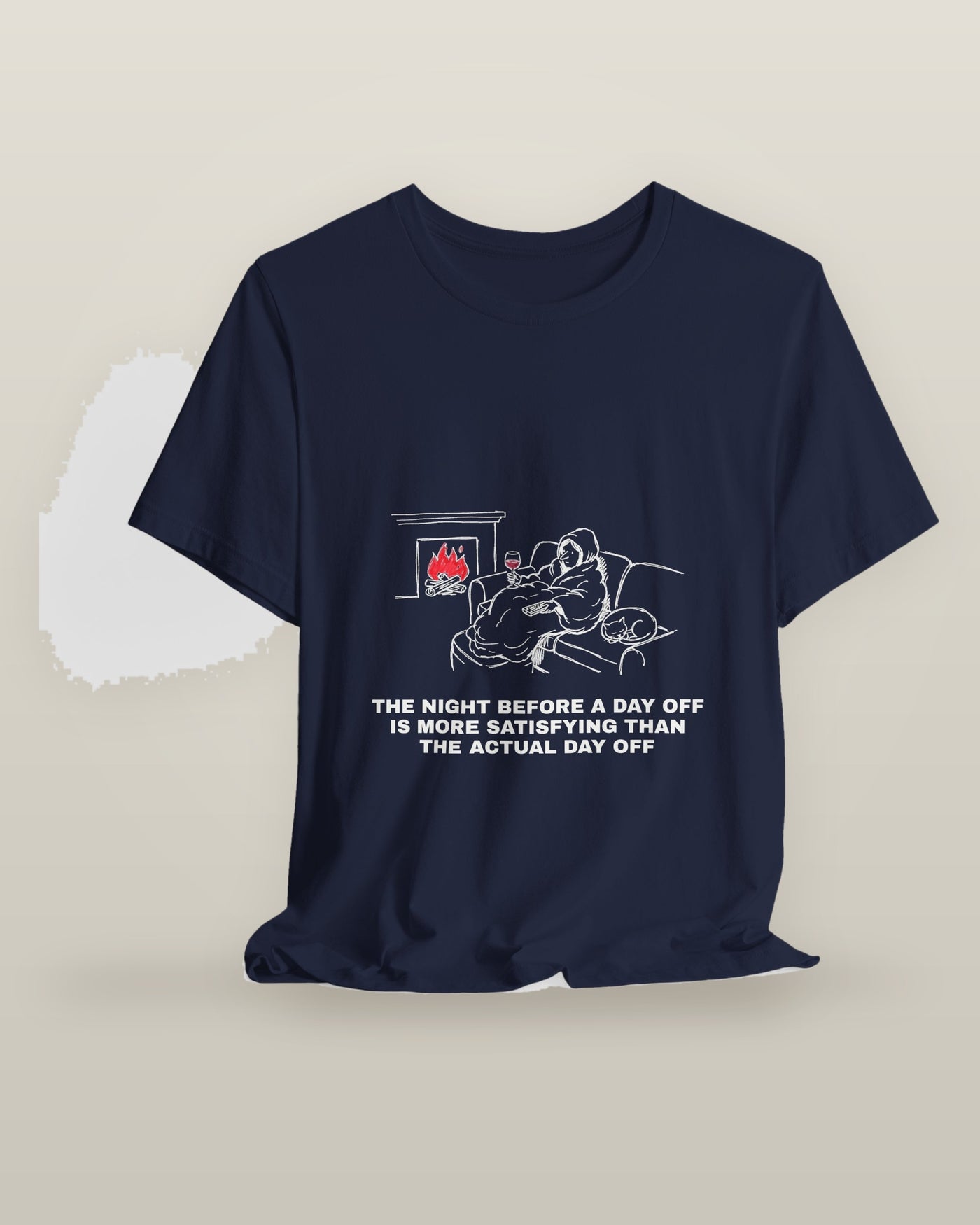 The night before a day off is more satisfying than the actual day off — a hooded figure under a blanket with wine, a remote, a sleeping cat and a lit fire, printed on a navy cotton t-shirt, on a hanger