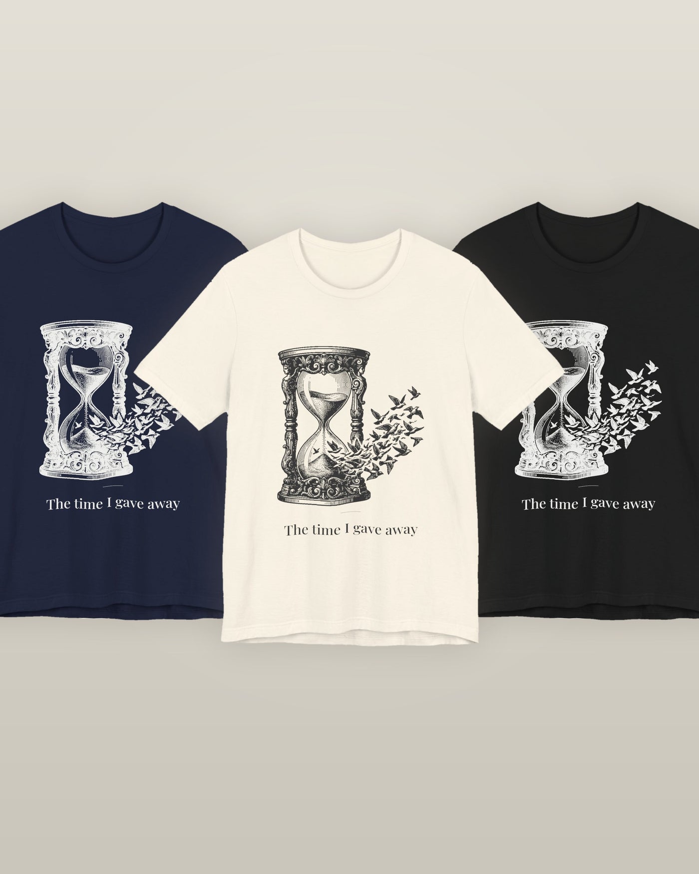 The time I gave away — an hourglass whose falling sand becomes a flock of birds, printed on a natural cream, navy and black cotton t-shirt, all three colourways together