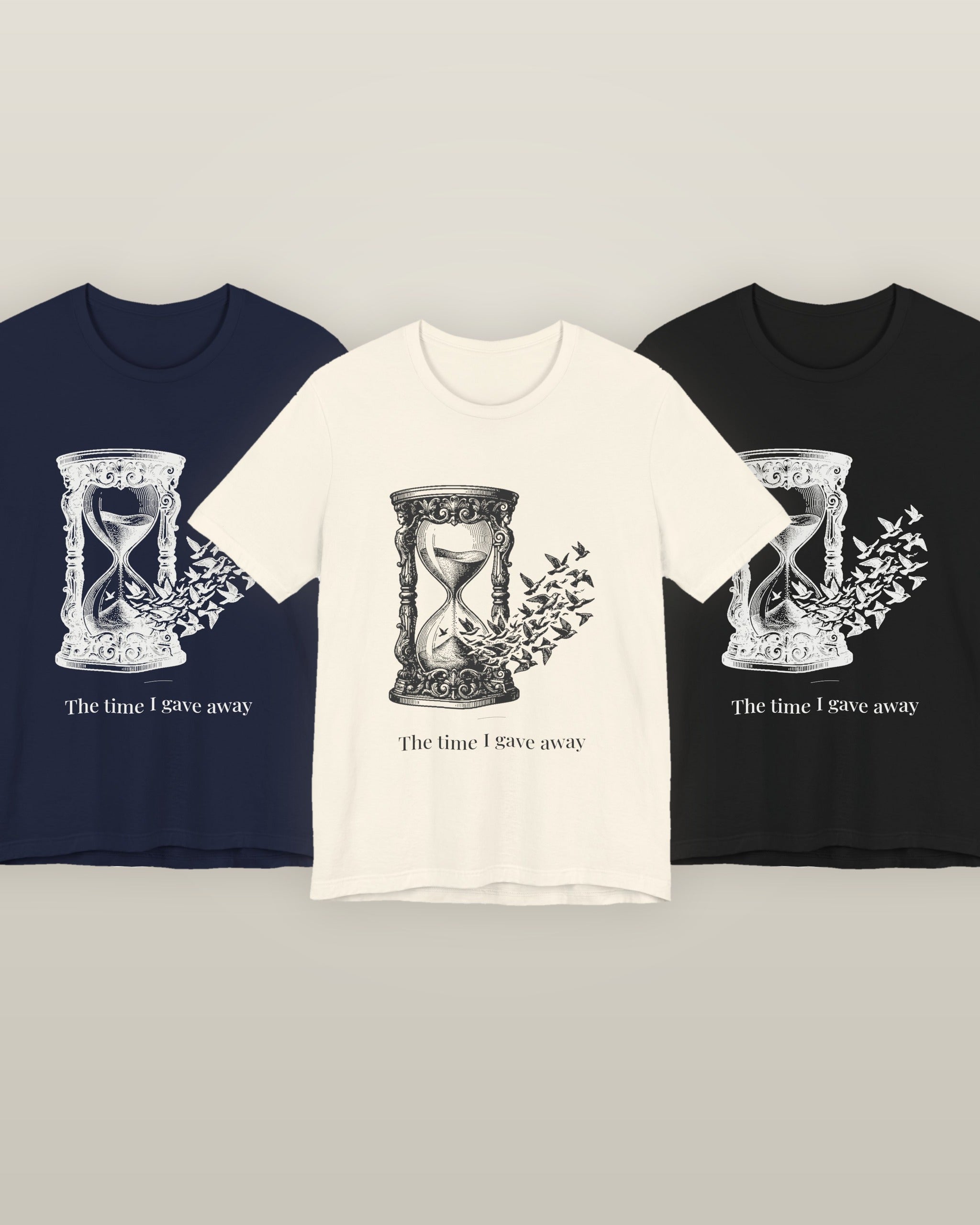 The time I gave away — an hourglass whose falling sand becomes a flock of birds, printed on a natural cream, navy and black cotton t-shirt, all three colourways together