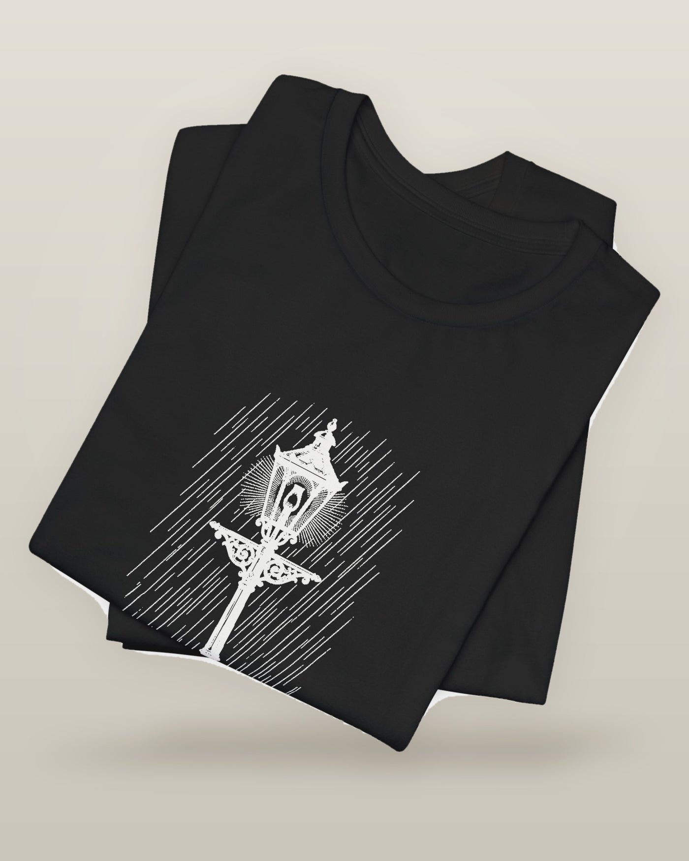 Still the only one awake — a cast-iron street lamp lit in fine rain, printed on a black cotton t-shirt, folded