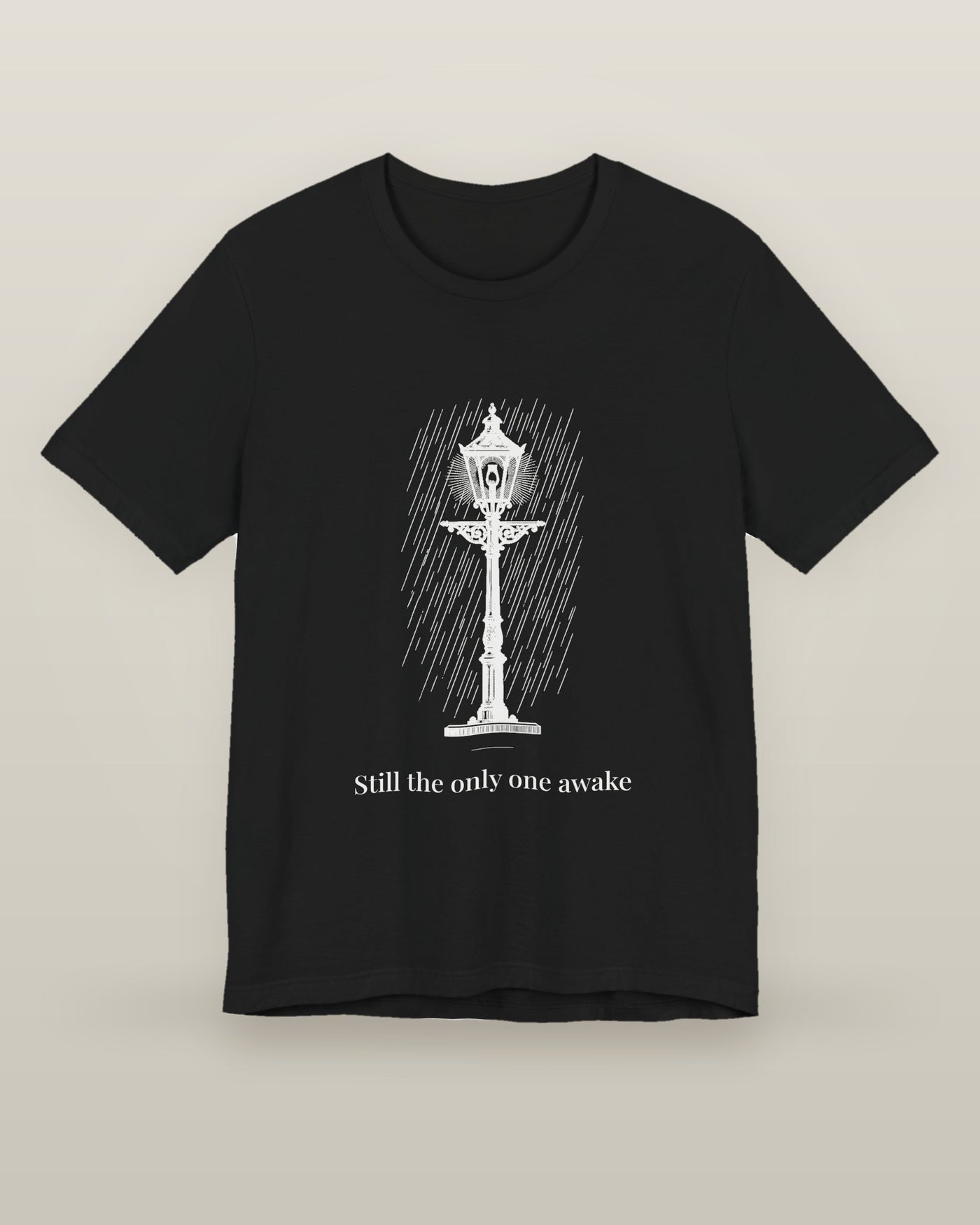Still the only one awake — a cast-iron street lamp lit in fine rain, printed on a black cotton t-shirt, front view