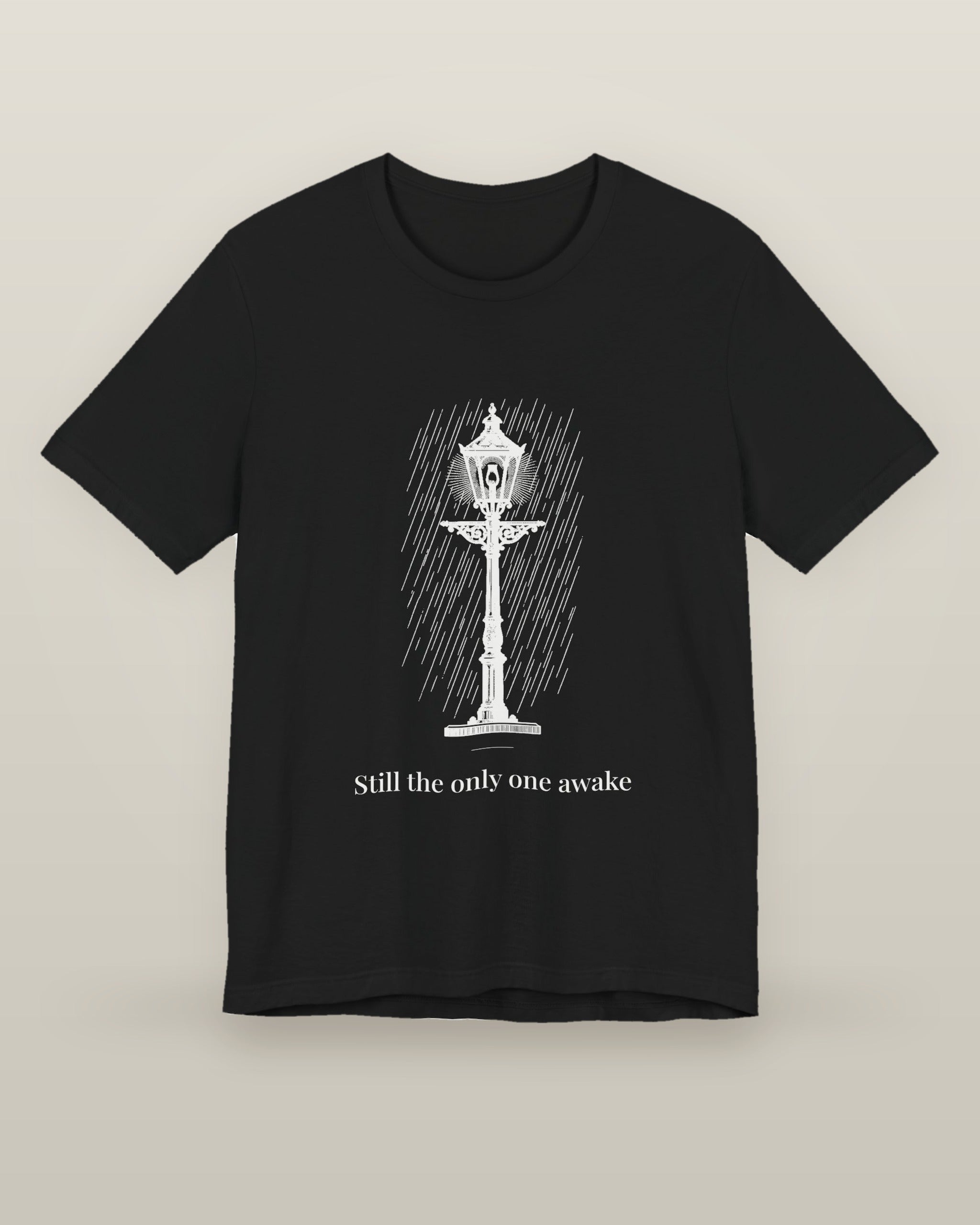 Still the only one awake — a cast-iron street lamp lit in fine rain, printed on a black cotton t-shirt, front view