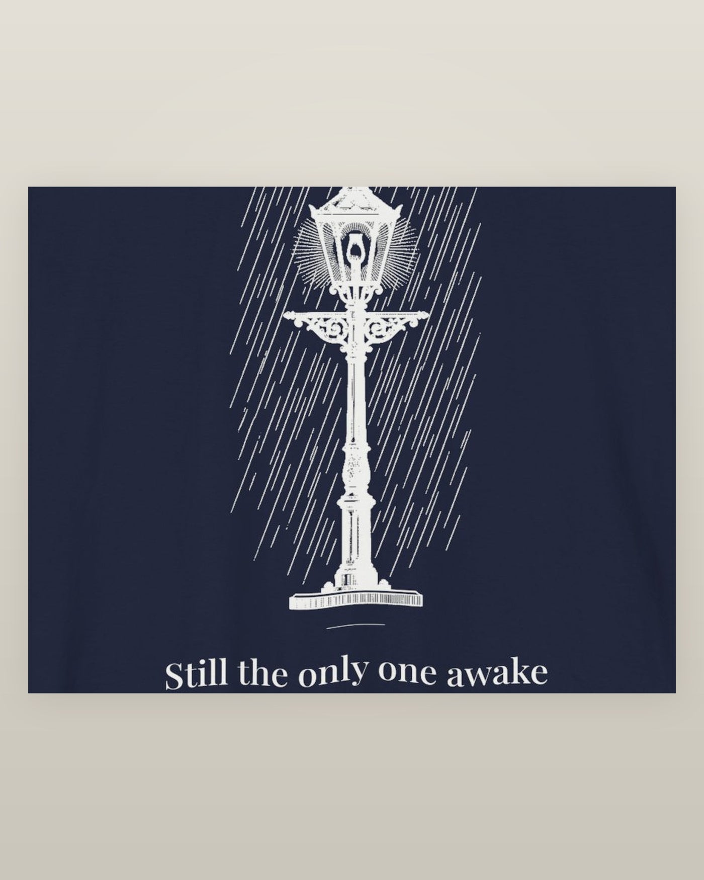 Still the only one awake — a cast-iron street lamp lit in fine rain, printed on a navy cotton t-shirt, close detail of the print