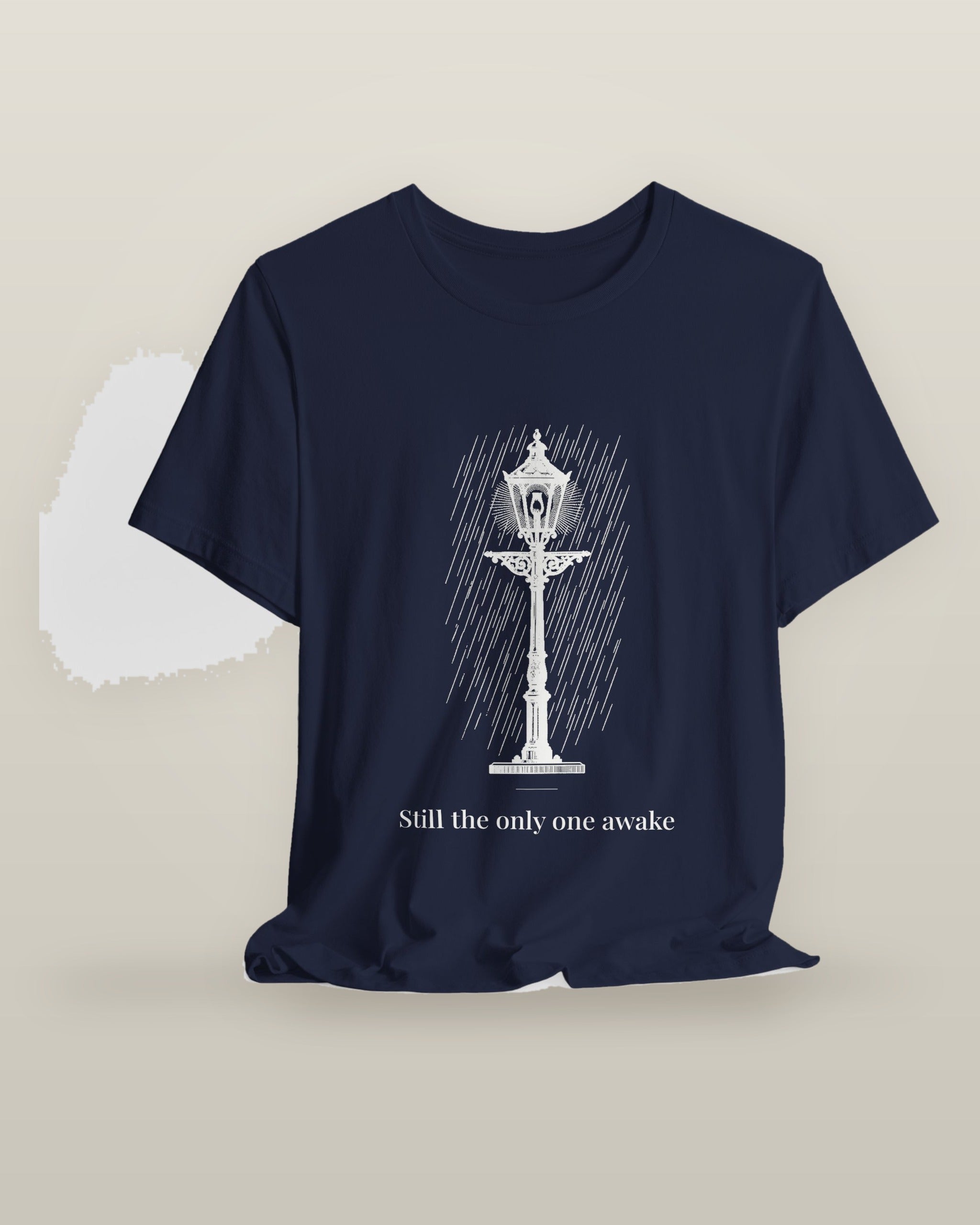 Still the only one awake — a cast-iron street lamp lit in fine rain, printed on a navy cotton t-shirt, on a hanger
