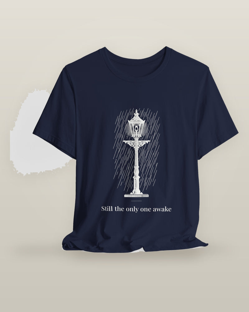 Still the only one awake — a cast-iron street lamp lit in fine rain, printed on a navy cotton t-shirt, on a hanger