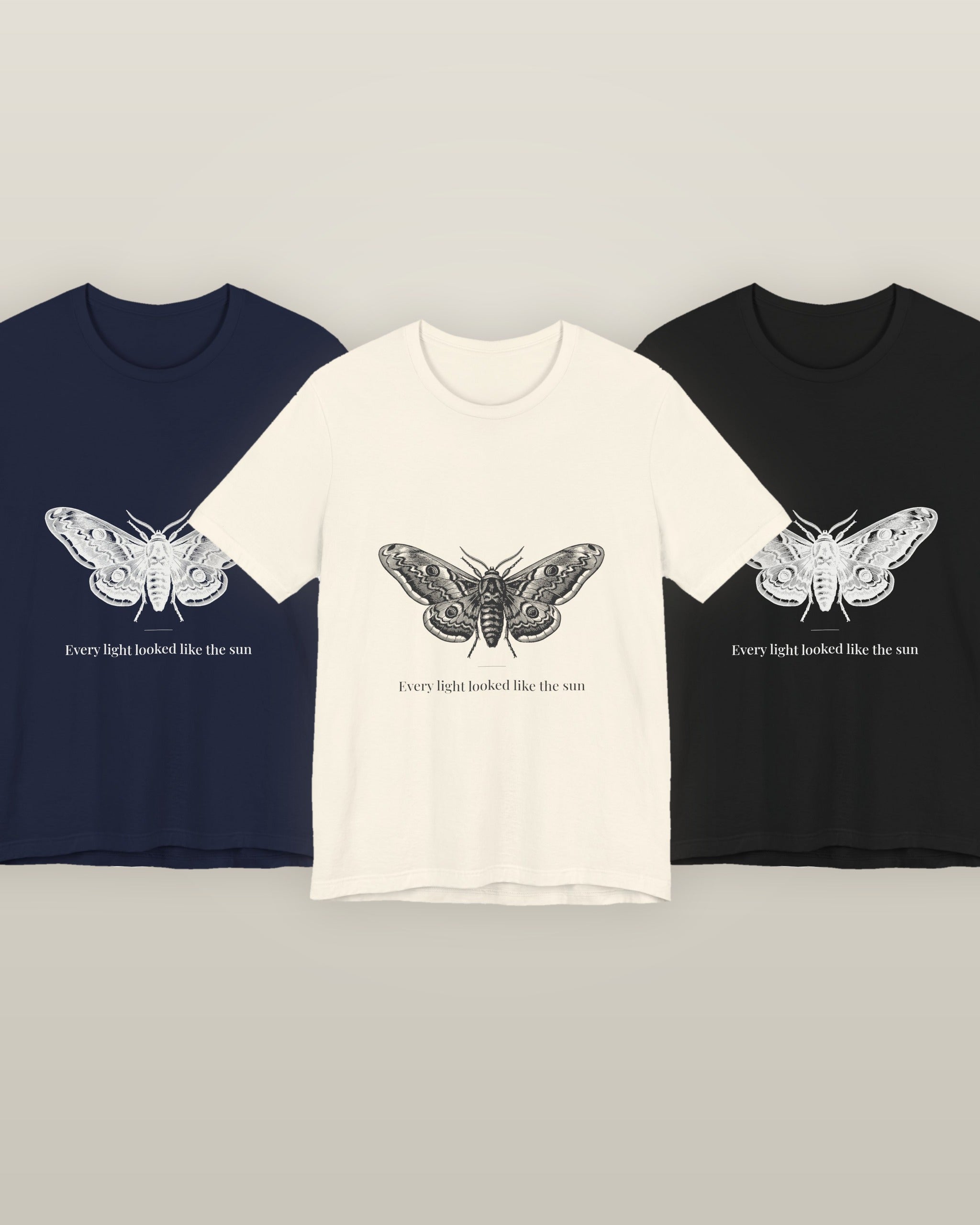Every light looked like the sun — a moth specimen study, wings spread, printed on a natural cream, navy and black cotton t-shirt, all three colourways together