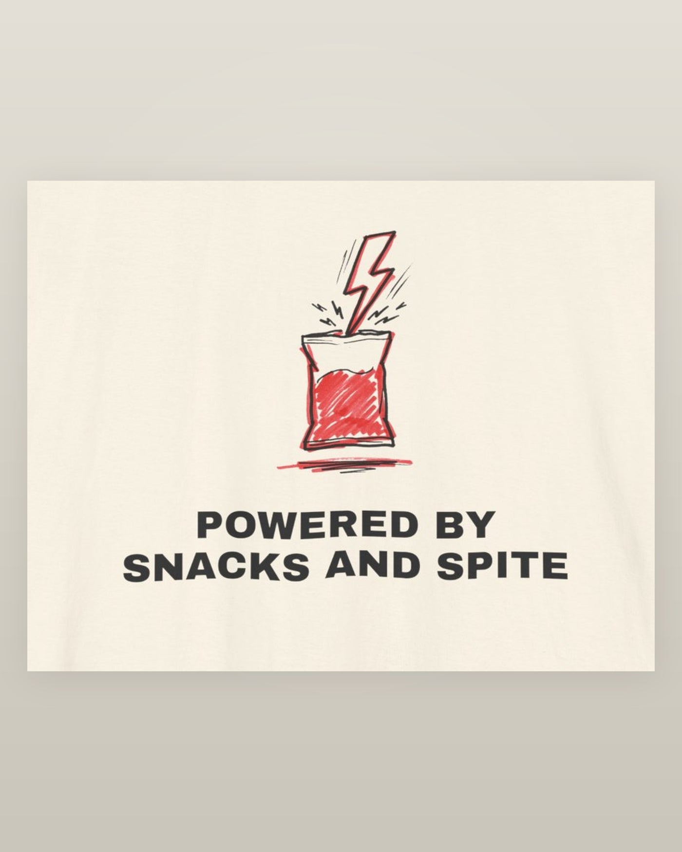 Powered by snacks and spite — a crisp packet struck by a lightning bolt, printed on a natural cream cotton t-shirt, close detail of the print
