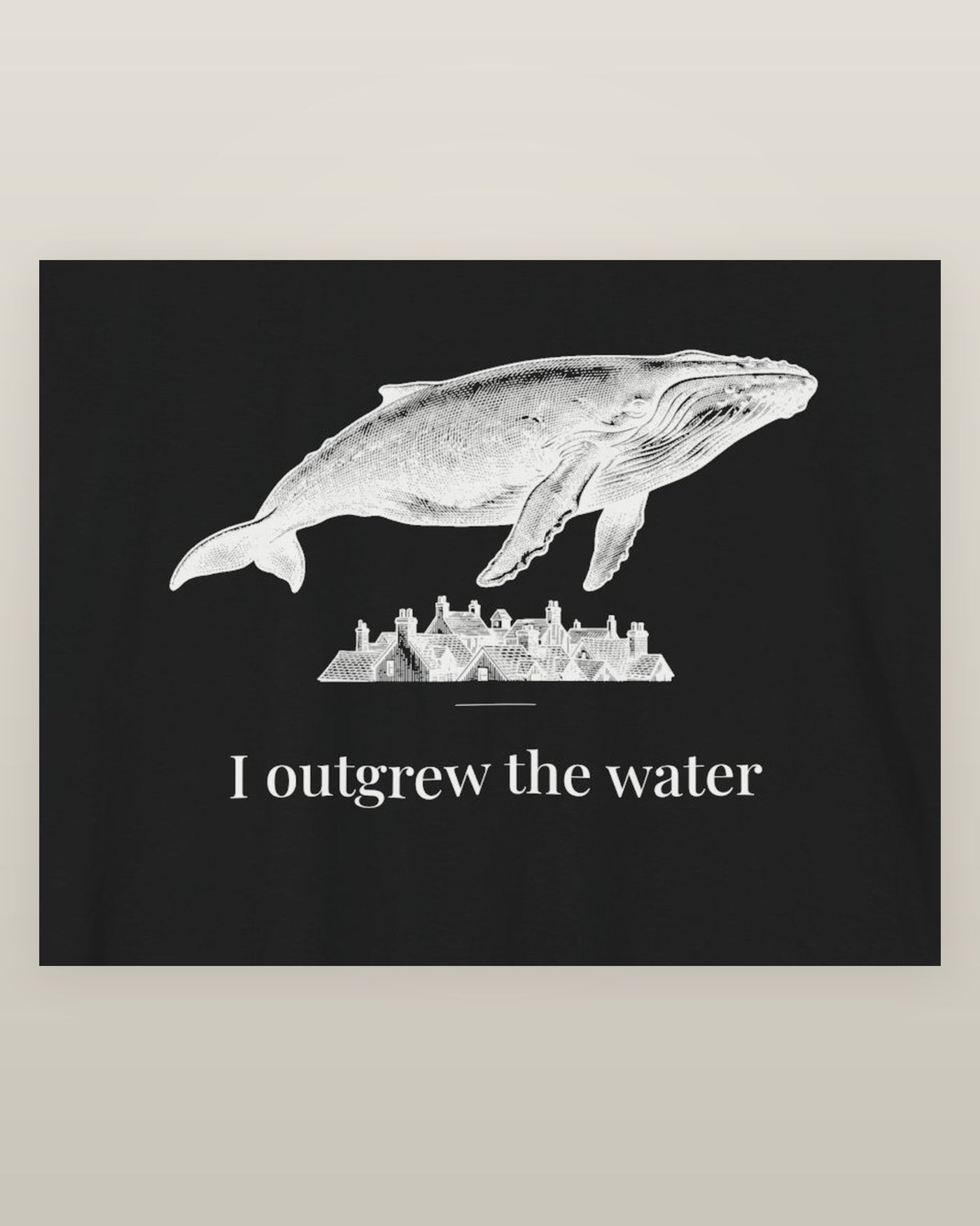 I outgrew the water — a humpback whale floating above rooftops, printed on a black cotton t-shirt, close detail of the print