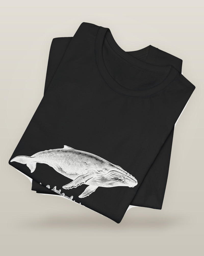 I outgrew the water — a humpback whale floating above rooftops, printed on a black cotton t-shirt, folded