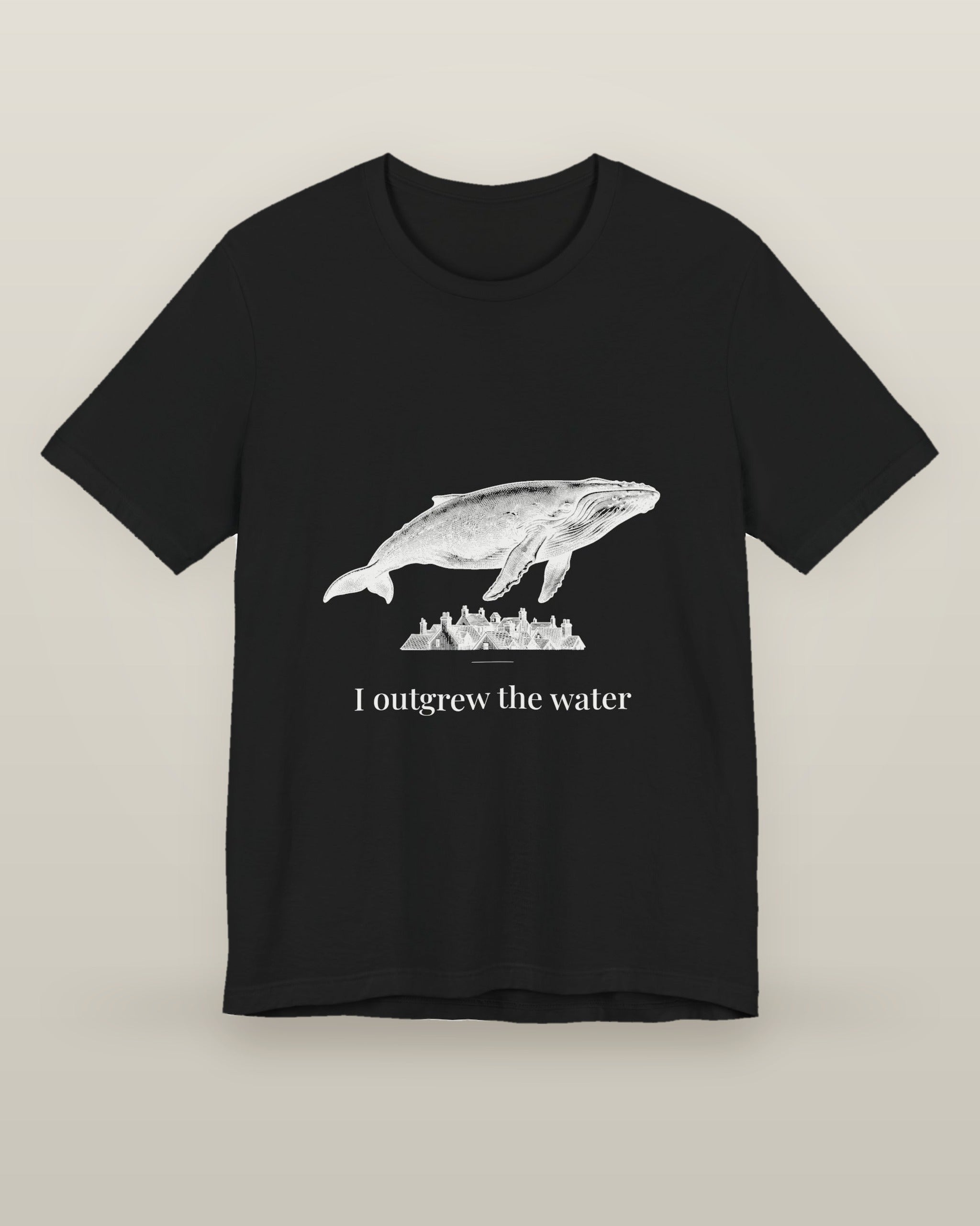 I outgrew the water — a humpback whale floating above rooftops, printed on a black cotton t-shirt, front view