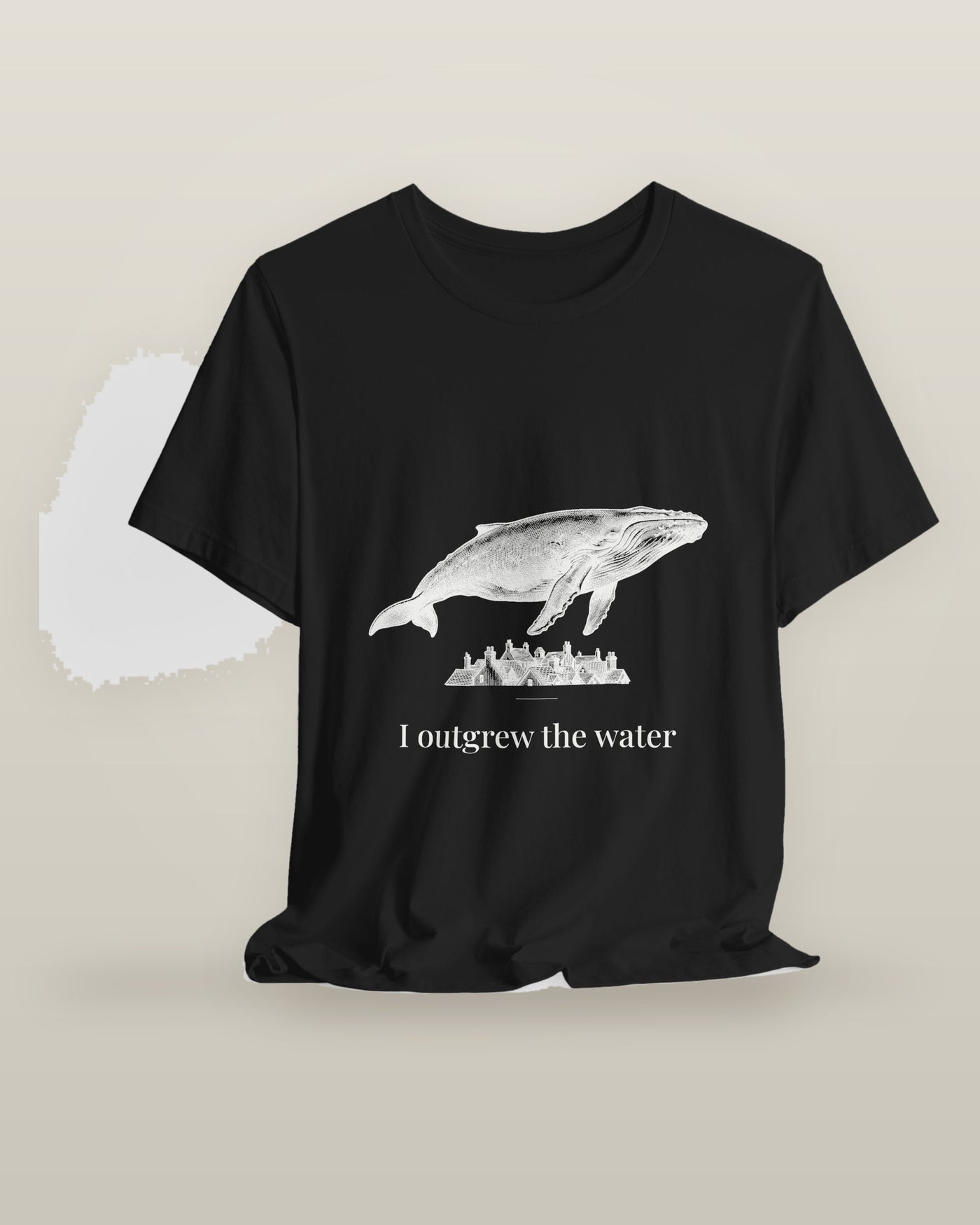 I outgrew the water — a humpback whale floating above rooftops, printed on a black cotton t-shirt, on a hanger