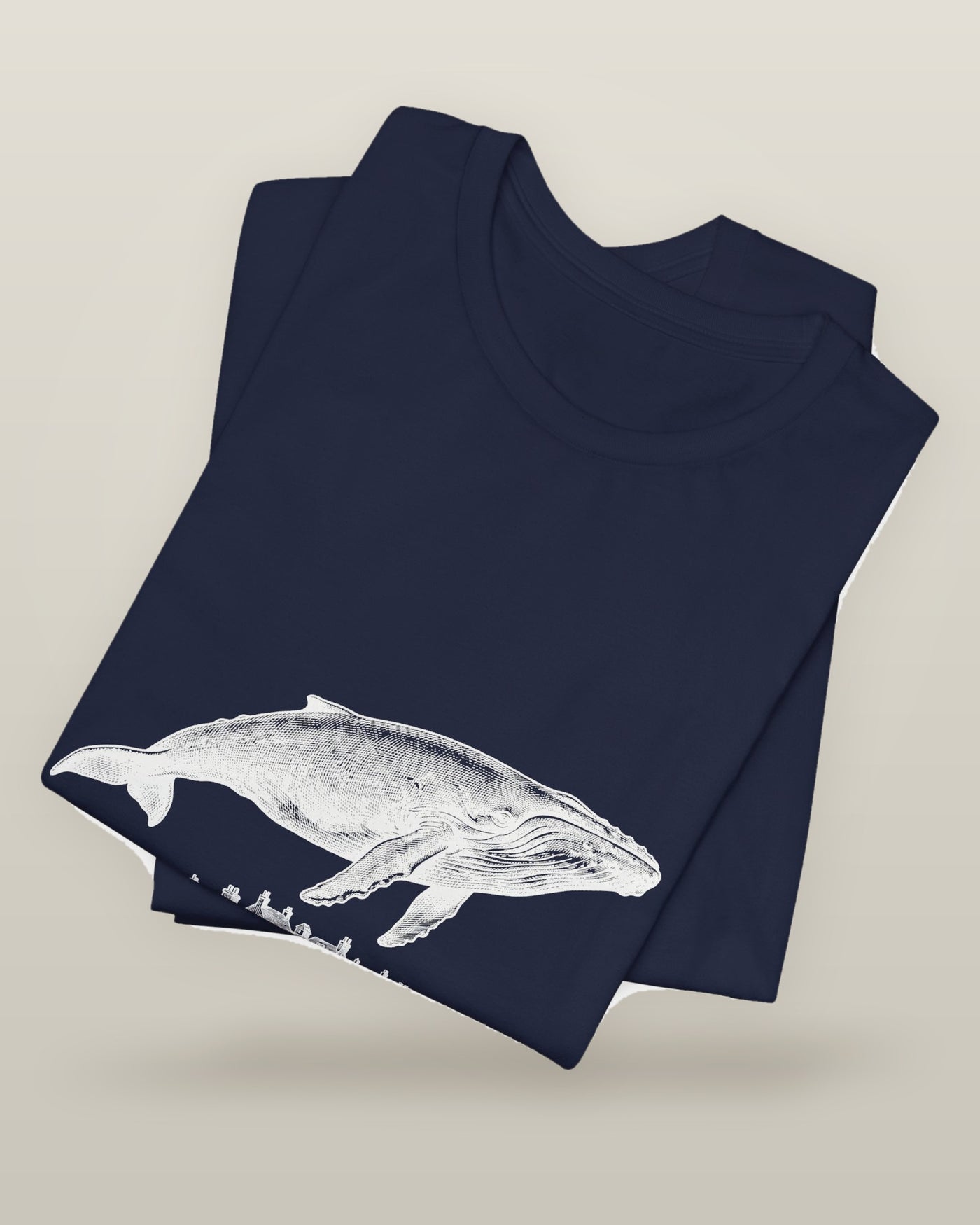 I outgrew the water — a humpback whale floating above rooftops, printed on a navy cotton t-shirt, folded